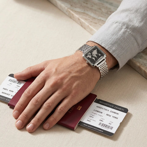 Men's waterproof square watch with black reflective world map dial Woodstock Zambon worn on wrist holding passport and boarding passes