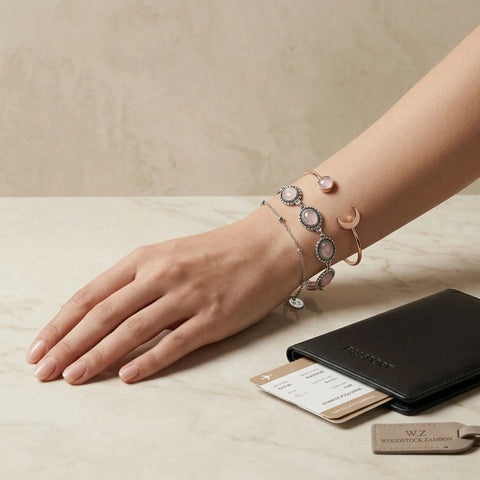 Wrist wearing stacked moonstone and crescent cuff bracelets in rose-gold and silver next to a passport and boarding pass — stackable moonstone bracelet set for travel, boho luxury jewelry