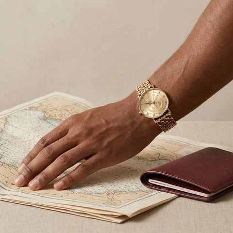 Men's gold anchor watch with nautical design on wrist over vintage map and leather wallet