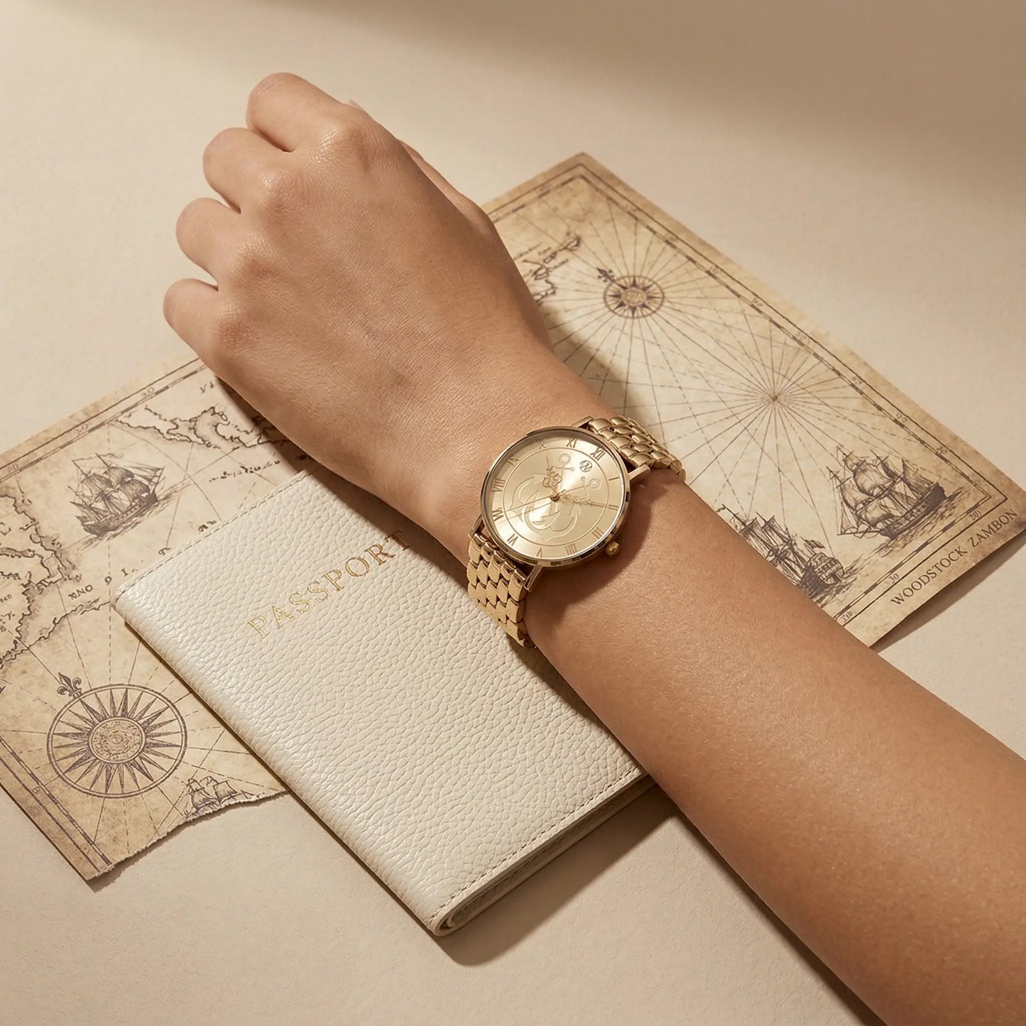 Women’s gold nautical anchor watch on wrist with travel passport and vintage sea map background