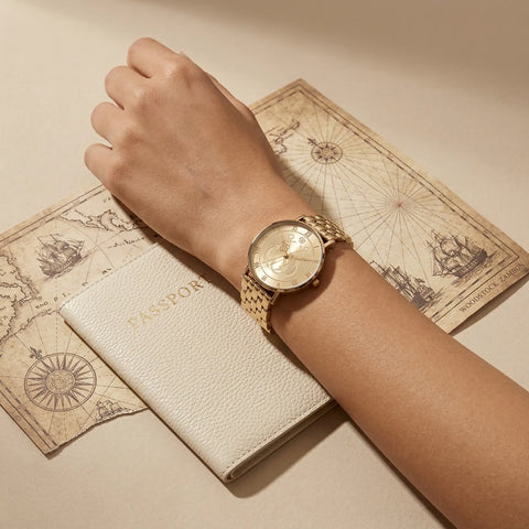Women’s gold nautical anchor watch on wrist with travel passport and vintage sea map background