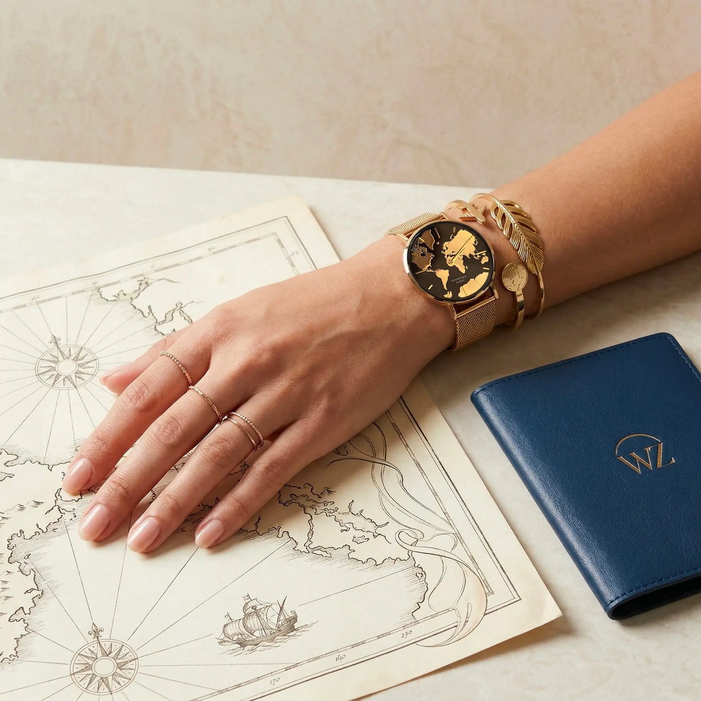 Gold world map watch with matching bracelets by Woodstock Zambon worn on wrist over vintage map with travel accessories