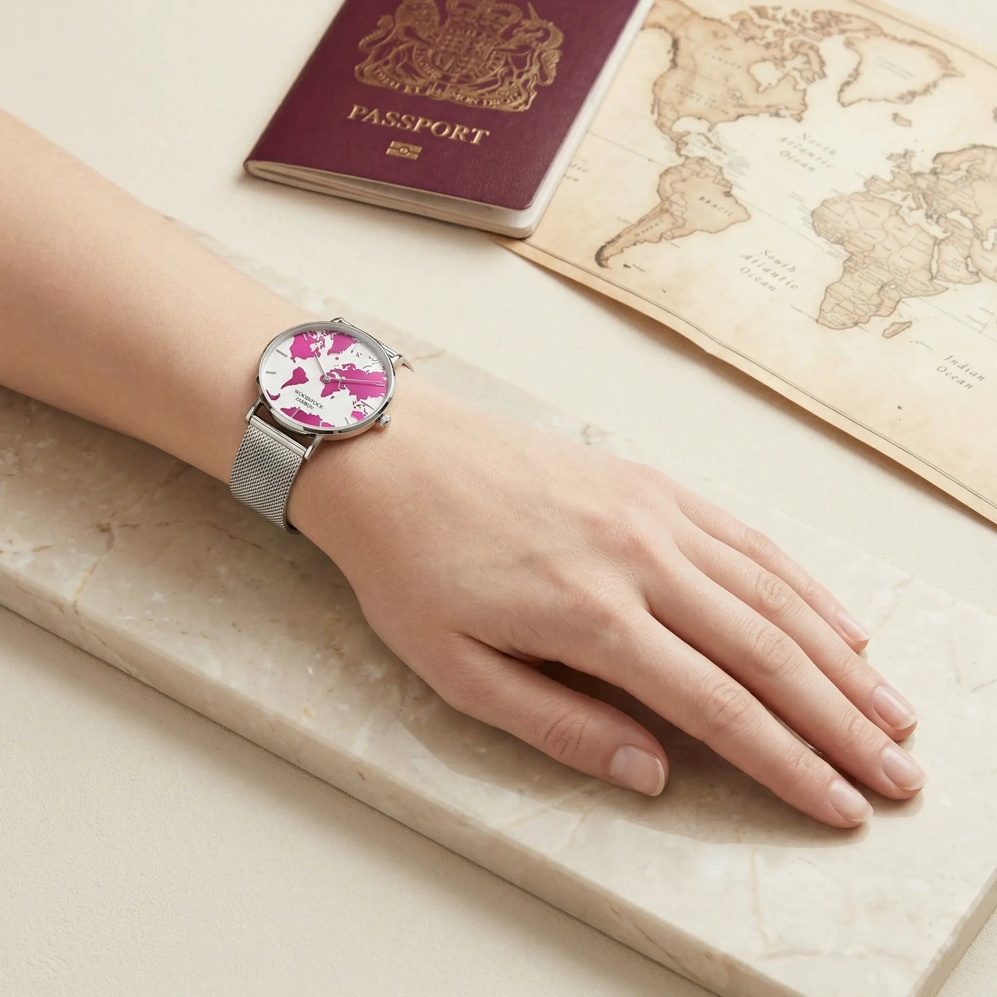 Women's pink world map watch Woodstock Zambon worn on wrist with passport and vintage world map