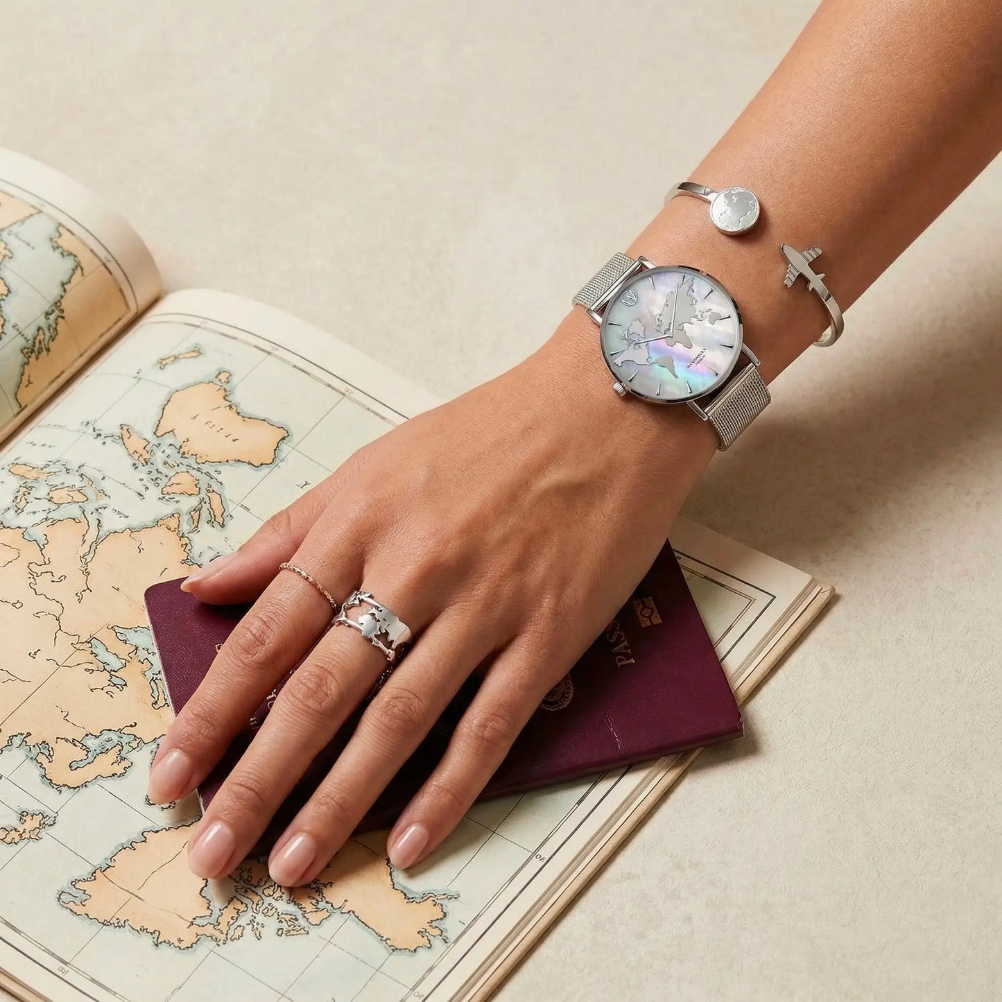 Silver mother of pearl world map watch with matching bracelets by Woodstock Zambon on wrist over vintage map and passport